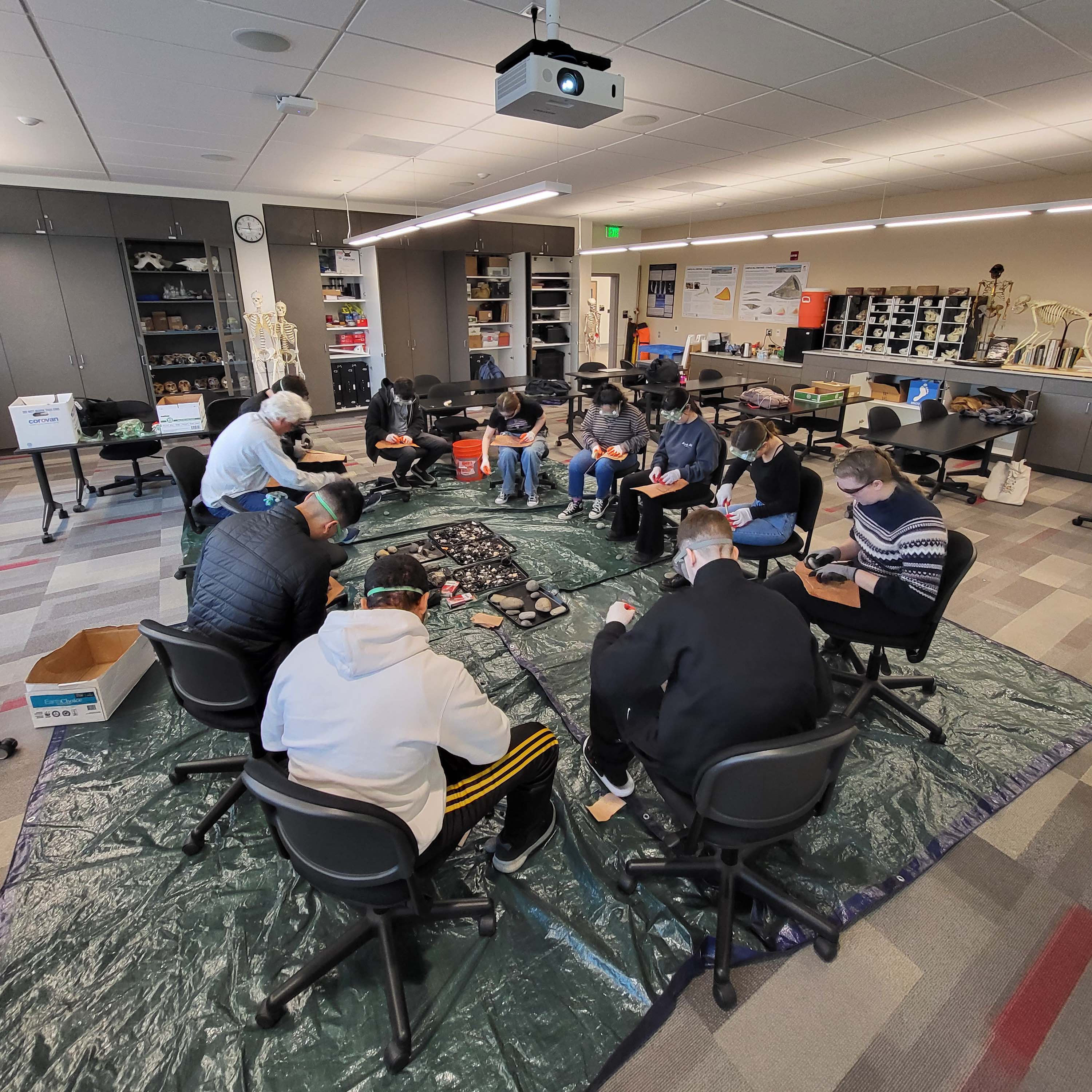 Class gathered in a circle flintknapping in the classroom.