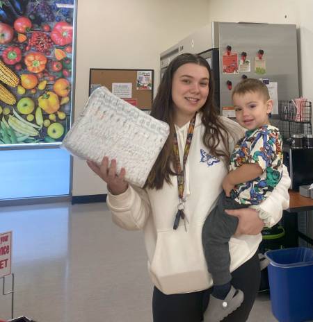 student parent holding diapers from the market and a baby