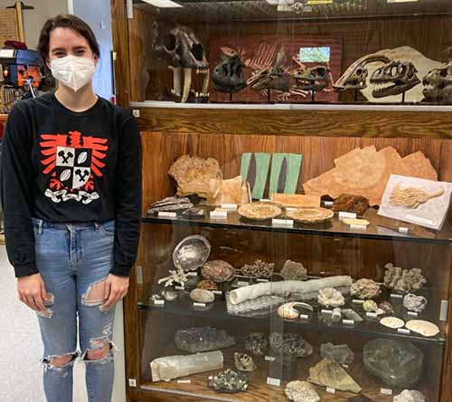 Geology student assistant standing next to the display case she built